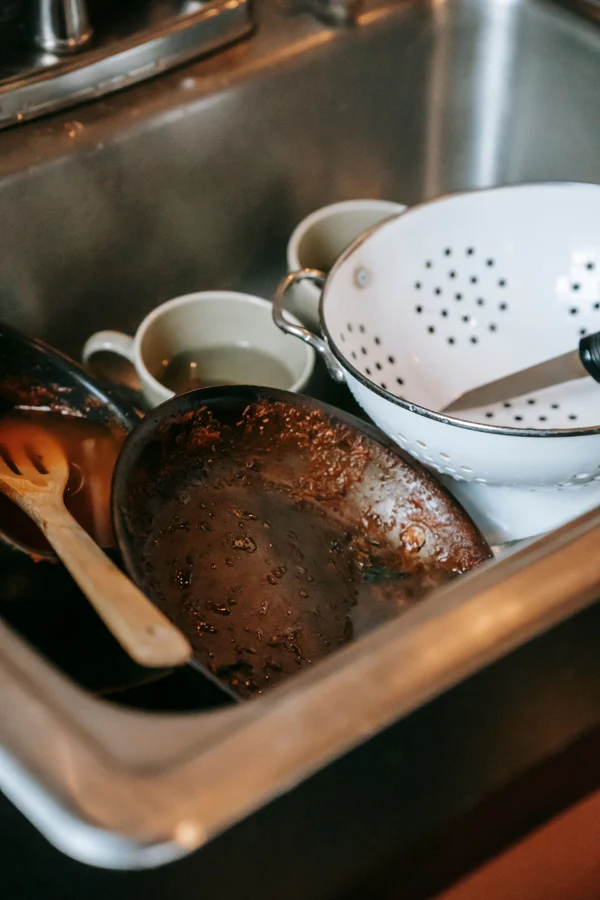 Everyday pots, mugs and utensils piled in a real sink